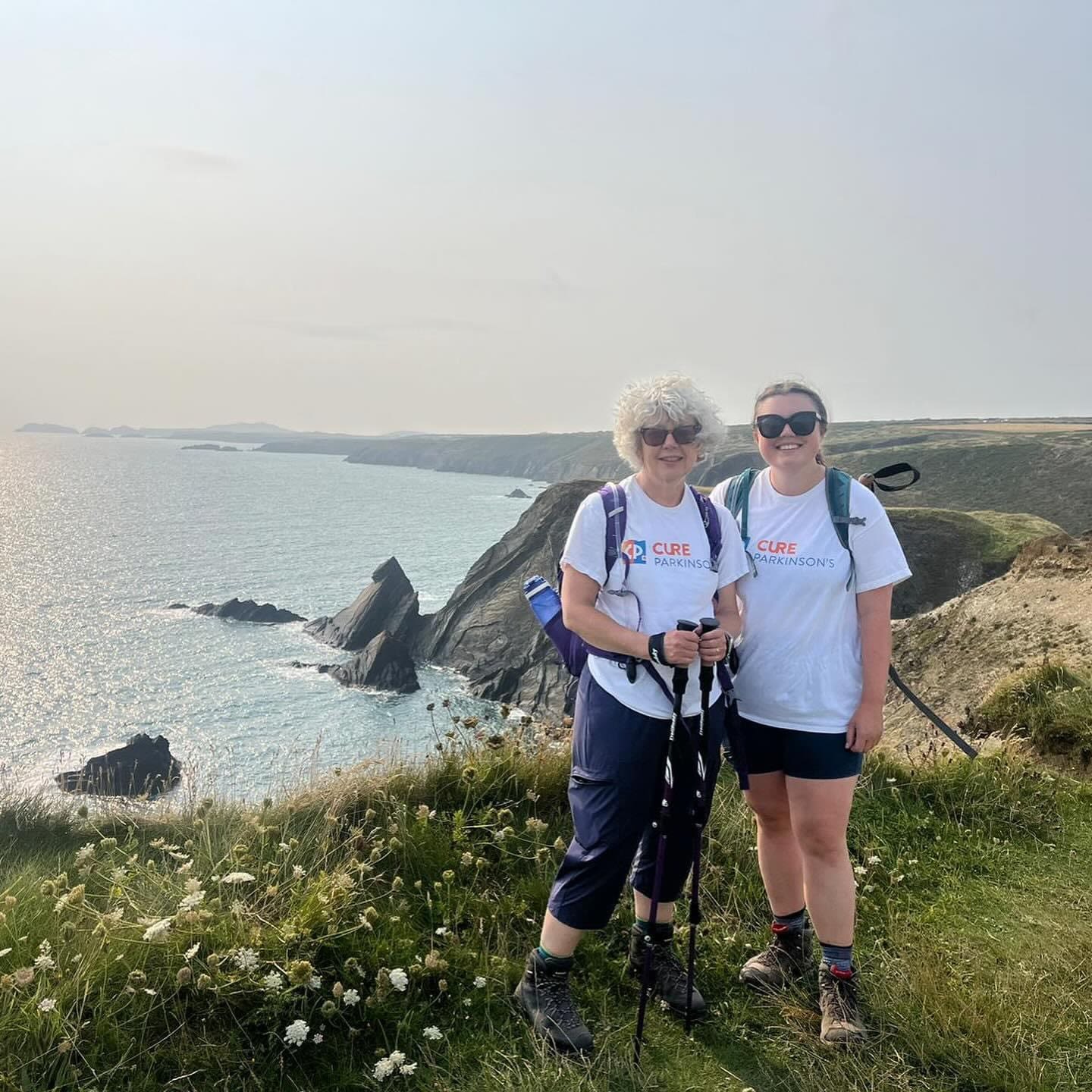Fundraisers Rebecca and Lily Whitehurst stand on cliffs by the coast in Cure Parkinson's t-shirts.