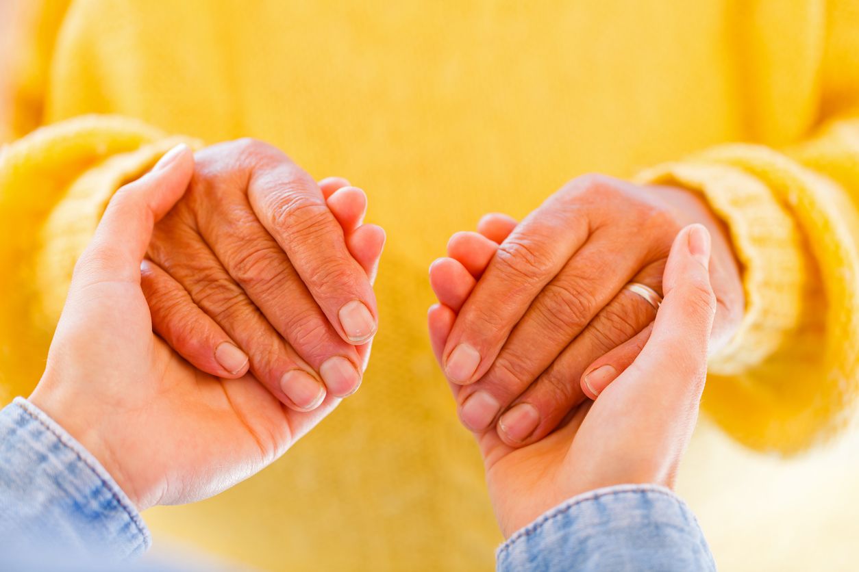 A pair of young woman's hands hold a pair of older woman's hands in a yellow wool sweater.