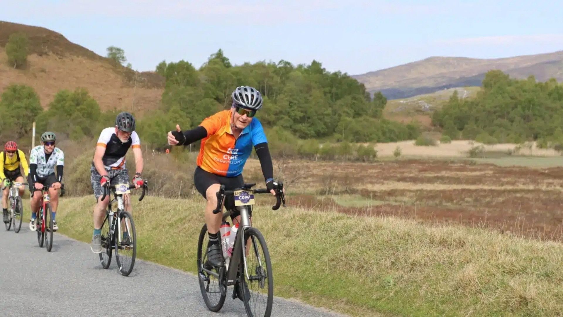 A cyclist in a Cure Parkinson's cycling vest riding through a field.